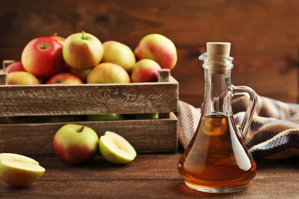 Apfelessig in Glasflasche auf braunem Holztisch