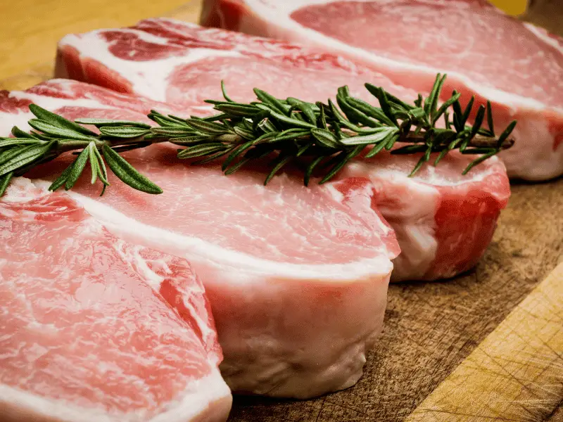 rohes schweinefleisch mit rosmarin auf einem brett